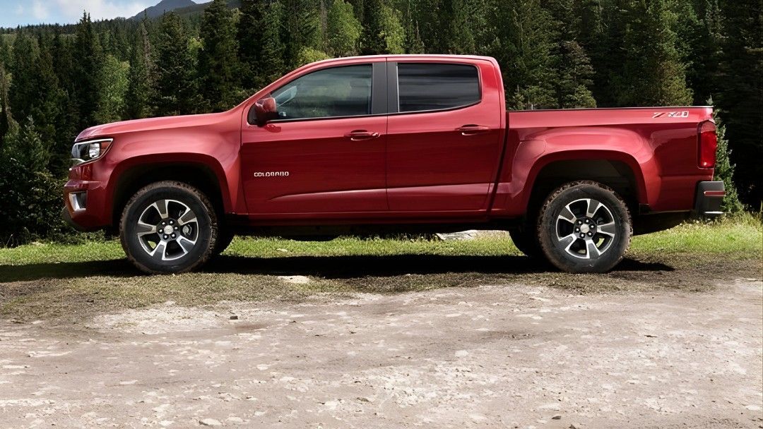 Chevrolet Colorado rouge 2015 stationné en nature, illustrant un camion usagé robuste et polyvalent.
