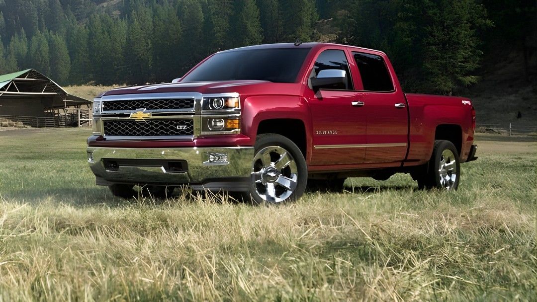 Chevrolet Silverado rouge 2014 garé dans un champ avec une grange en arrière-plan, représentant un pickup durable et puissant.