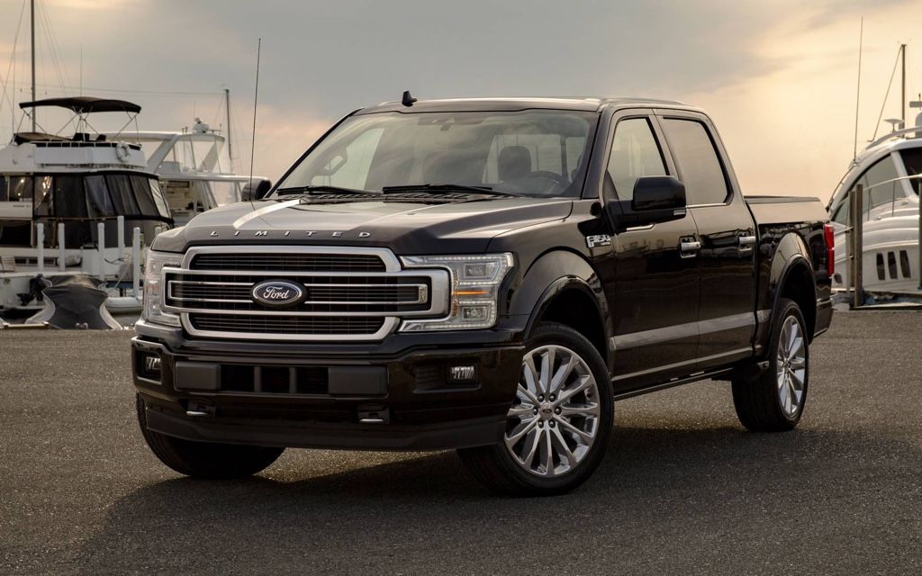 Ford F-150 2020 noir stationné près d’un quai de marina au coucher du soleil, symbole de puissance et de prestige.